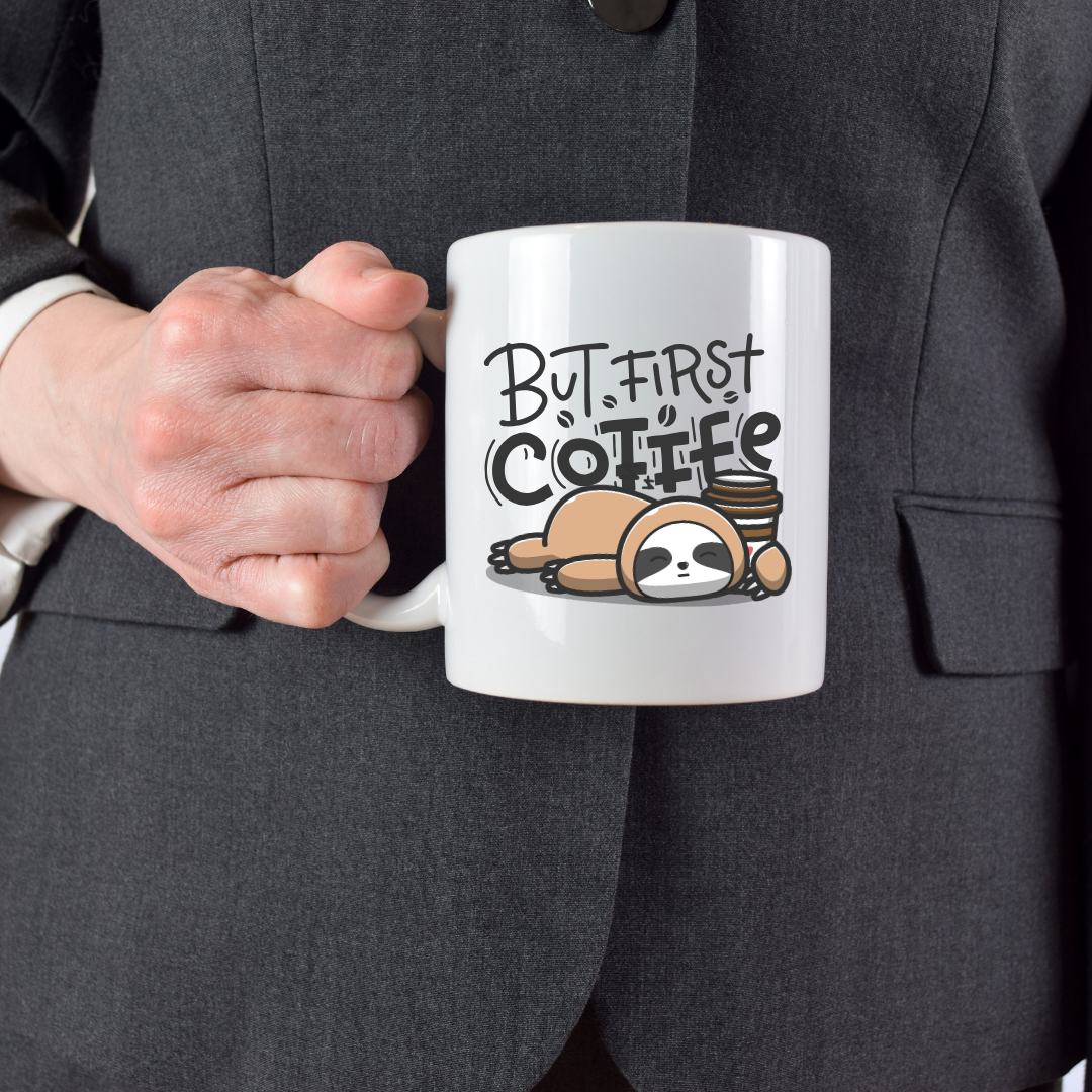 Person holding a mug with a sloth illustration and 'But First Coffee' text.