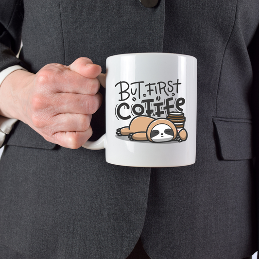 Person holding a mug with a sloth illustration and 'But First Coffee' text.