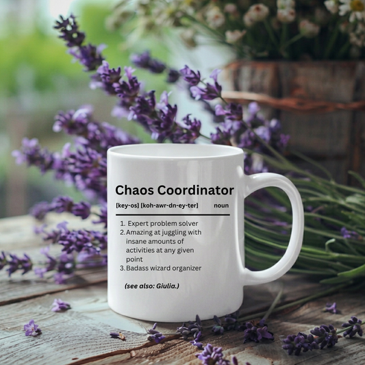 A white ceramic mug with a humorous dictionary-style definition for 'Chaos Coordinator' printed in black text, set on a rustic wooden surface surrounded by purple lavender flowers.