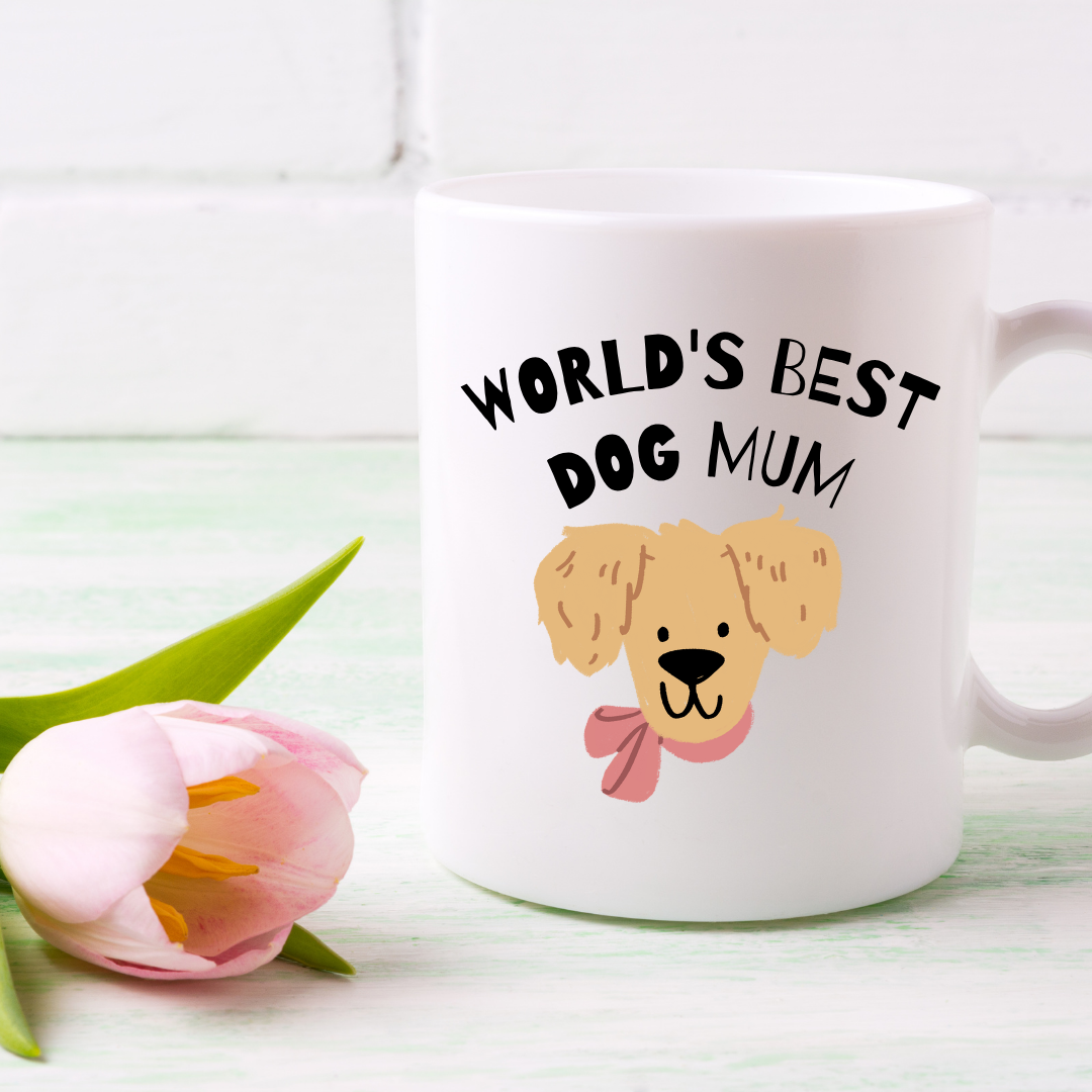 White mug with 'World's Best Dog Mum' text and dog illustration, next to a pink tulip on a light background